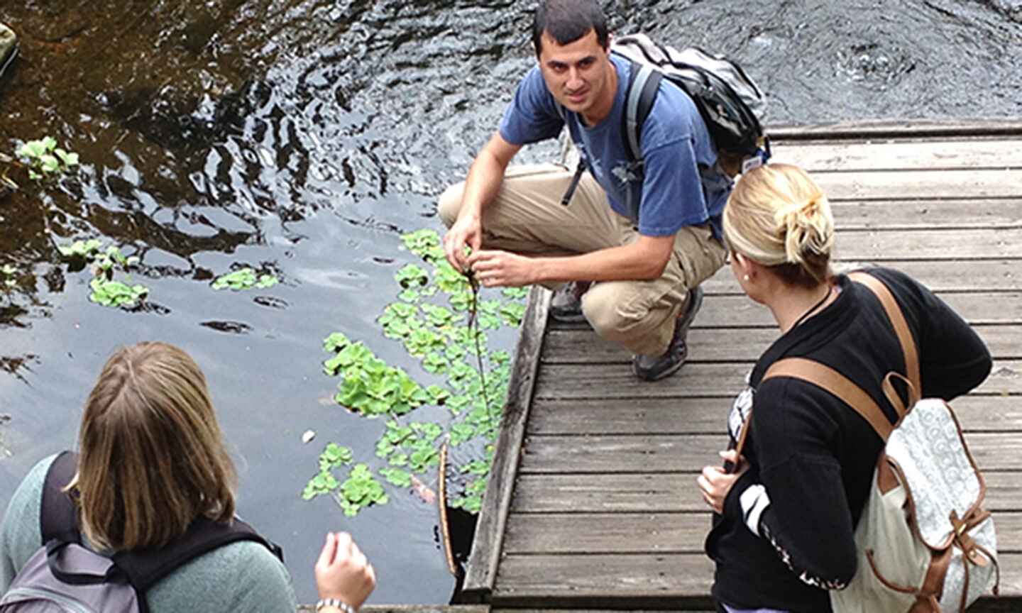 Three people talking on a dock over a pond 