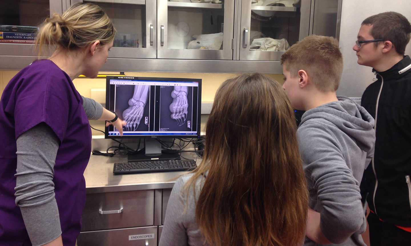 A nurse teaching three kids about a broken bone as they all look at a computer showing an X ray