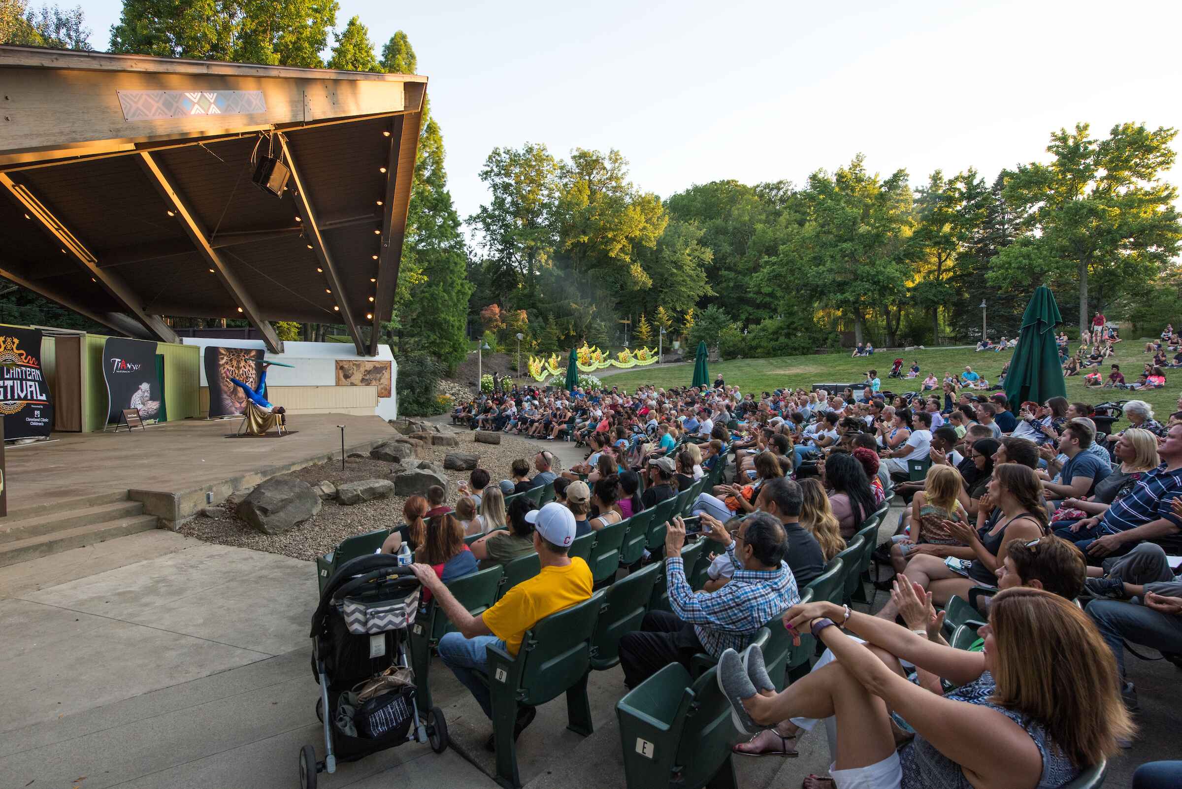 A bunch of people in the audience watching a performance at a wooden ampitheatre during the afternoon