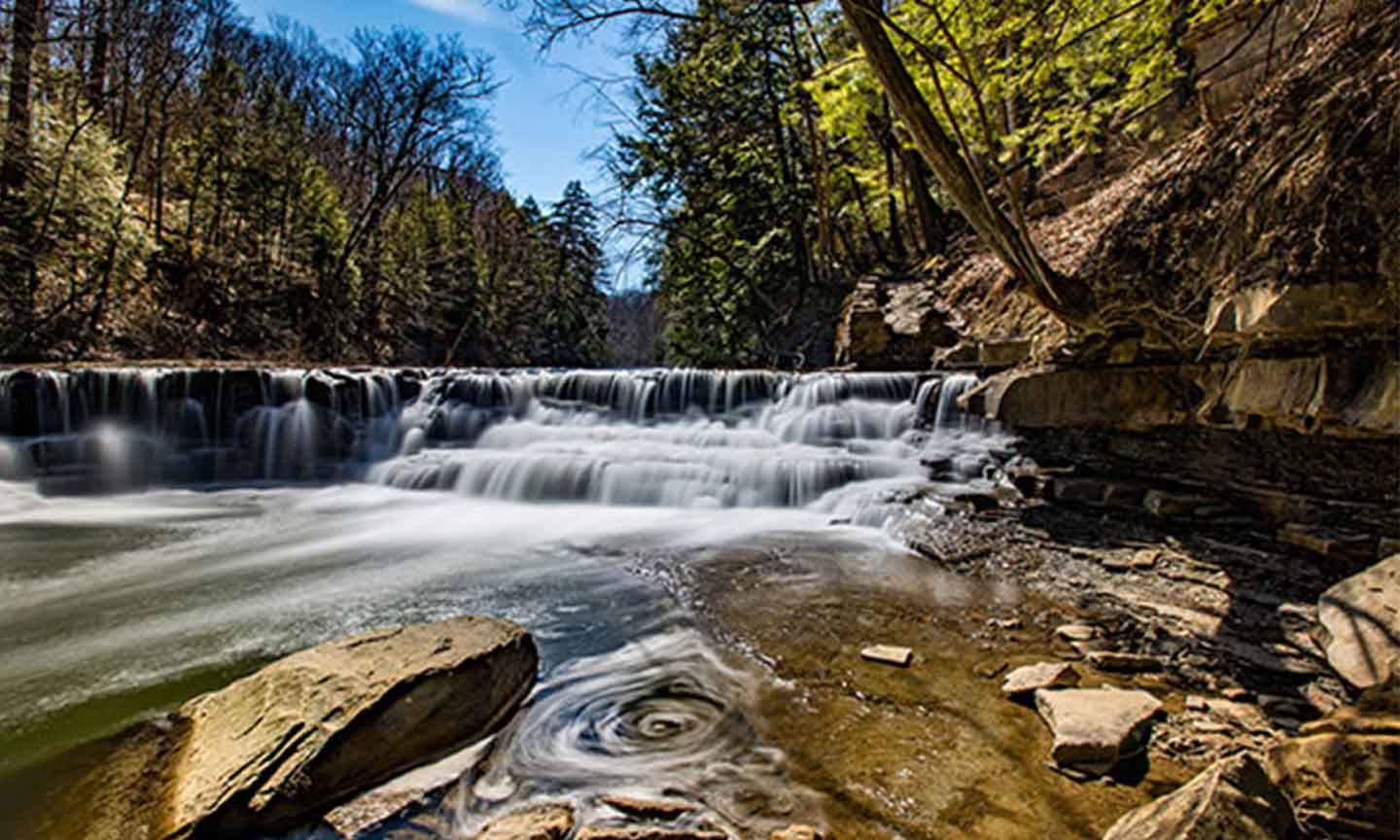 A beautiful waterfall tumbles over rocks, nestled among trees in a serene woodland landscape.