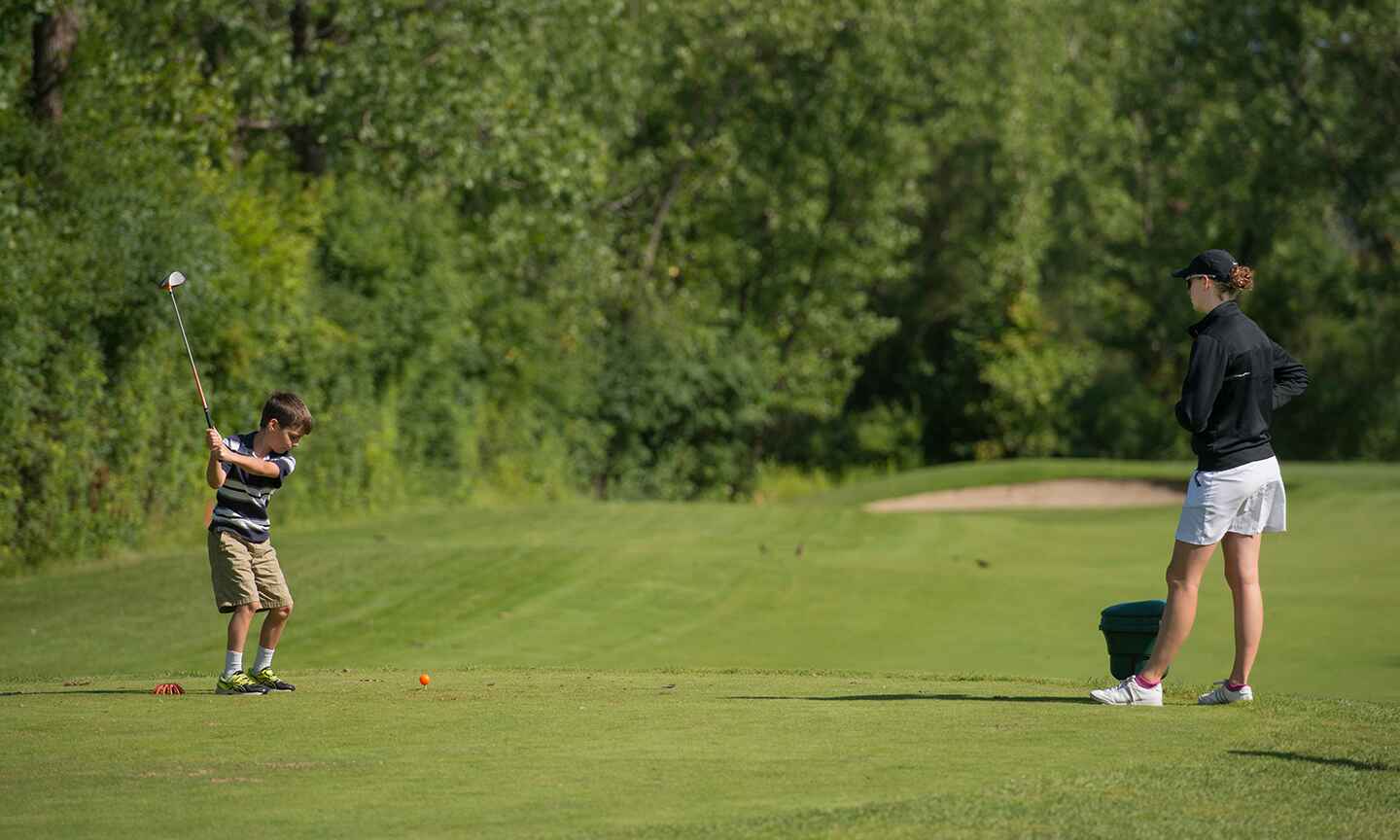 A young boy taking a swing with a golf club, with a coach standing nearby.