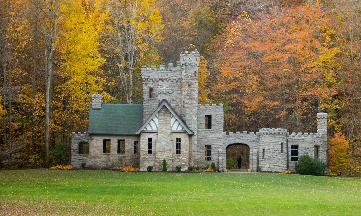 A small stone castle nestled in the woods, with autumn trees in shades of orange and yellow surrounding it.