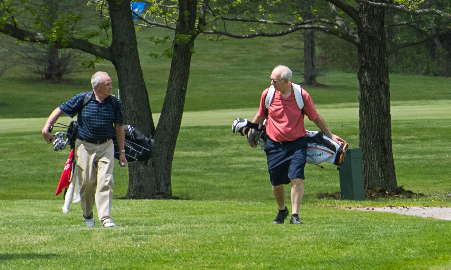 Two old men with golf equipment walking on a golf course