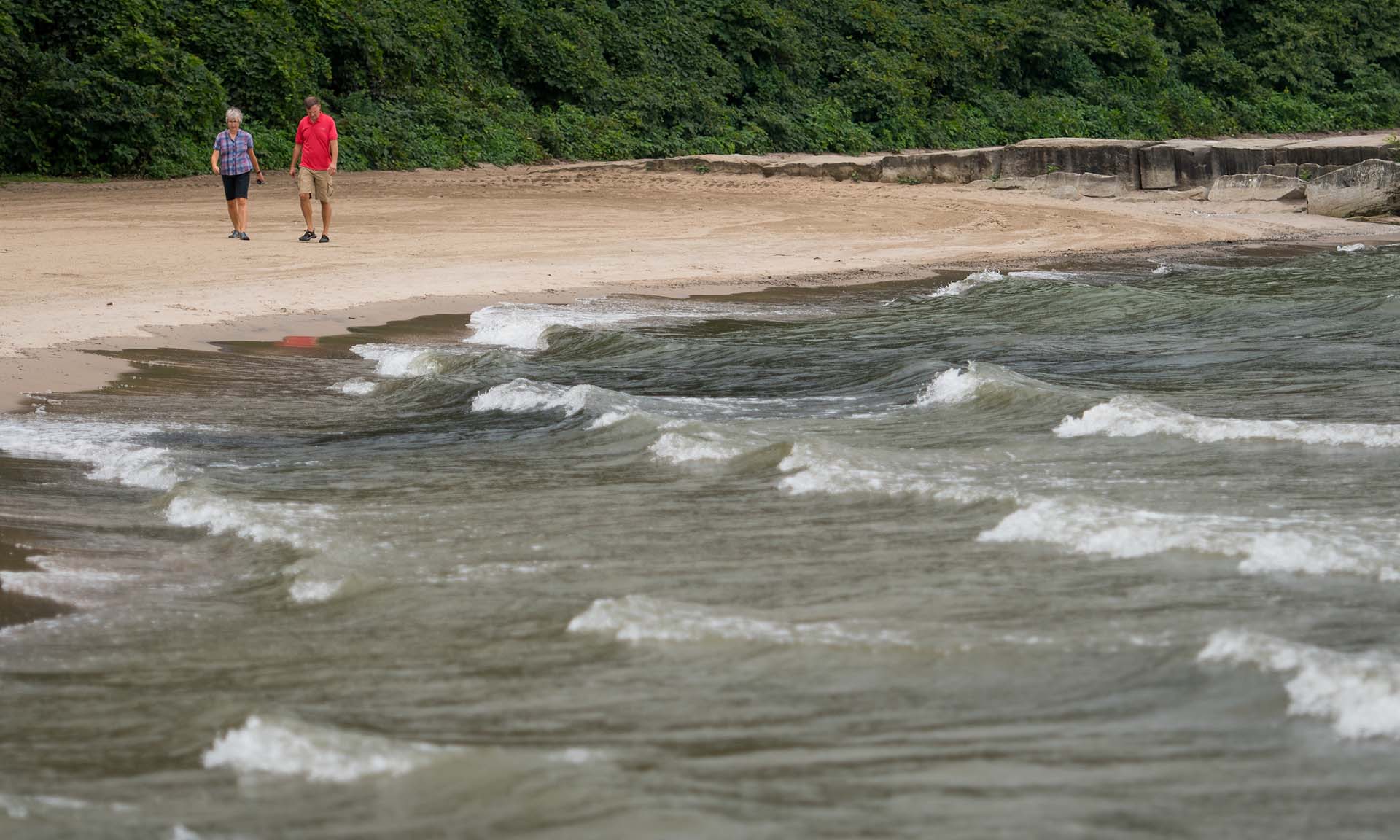 Two individuals stroll along the tranquil shore of a serene lake, enjoying the peaceful natural surroundings.