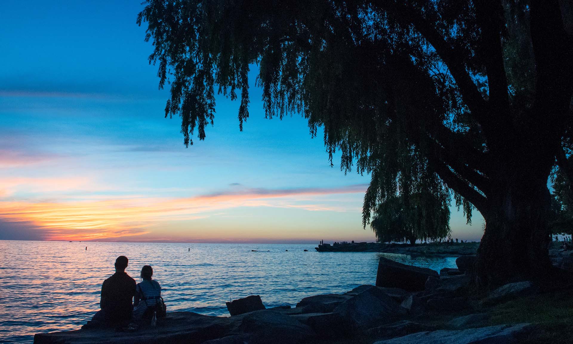 People sitting on a rock and watching the sunset over the water