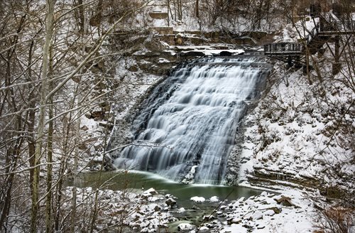 A stunning waterfall tumbles down in a snow-covered forest, creating a peaceful winter landscape.