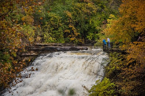 A couple stands on a bridge, admiring a beautiful waterfall as it flows powerfully in the background.