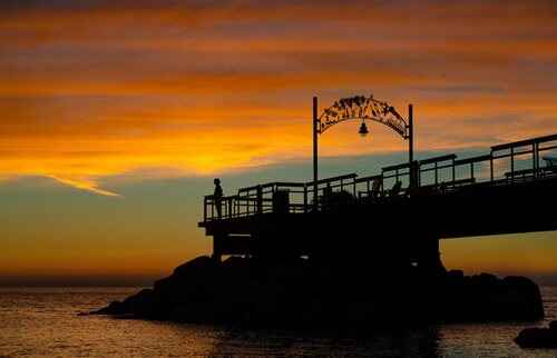 A serene sunset over a pier featuring a bridge and a sign, casting warm hues across the water.