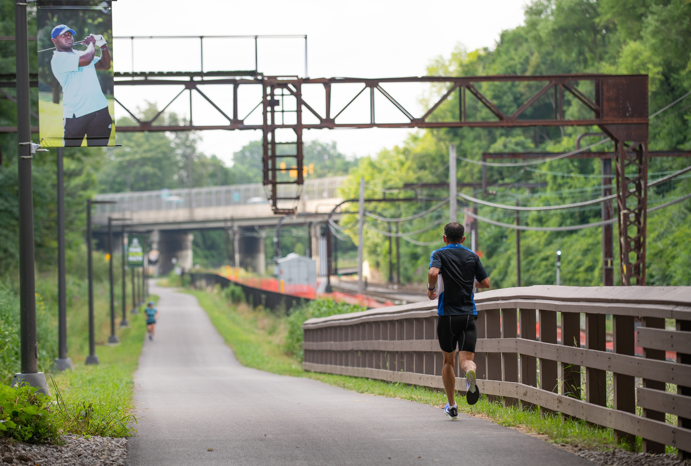  A man jogs on a path adjacent to a bridge, emphasizing fitness and the beauty of nature in the background.