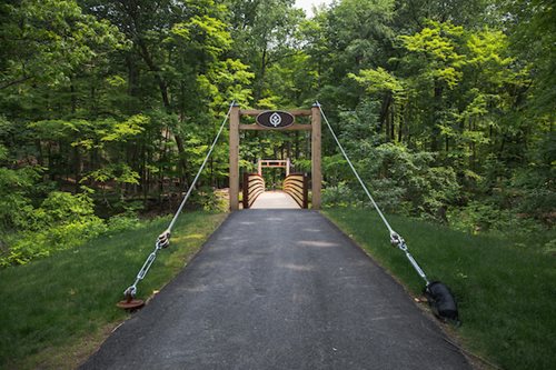 A charming bridge that opens up to a serene park, surrounded by greenery and tall trees, ideal for relaxation and recreation.