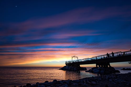 A picturesque sunset over a pier, with a clear blue sky and fluffy clouds enhancing the scenic view.