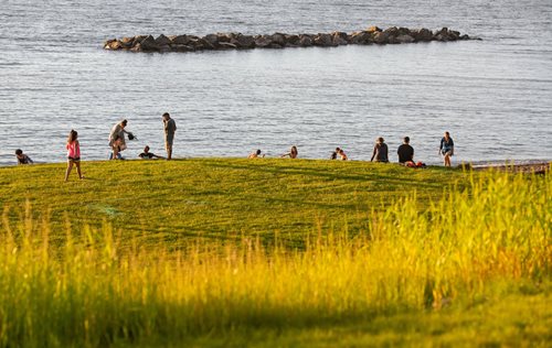 people are walking on a grassy hill near the water, a photo by Svend Rasmussen Svendsen, shutterstock contest winner, ecological art, people resting on the grass, parks and public space, grassy hill