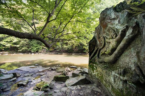 A stone carving depicting a woman seated on a rock beside a flowing river, showcasing intricate details and serene surroundings.