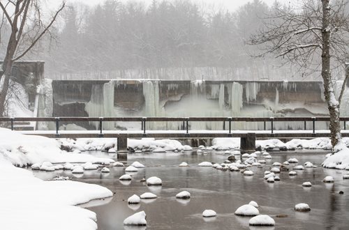 snowy scene of a bridge over a river with a waterfall in the background, a picture by Shirley Teed, shutterstock contest winner, hudson river school, frozen waterfall, ice seracs, wall of water either side