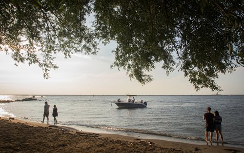 people are standing on the beach watching a boat pass by, a stock photo by Andrew Domachowski, instagram contest winner, regionalism, parks and lakes, cottage hippie naturalist, cottagecore