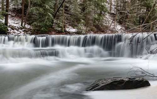 A stunning winter waterfall flowing amidst a snowy landscape, highlighting the peacefulness of the season.