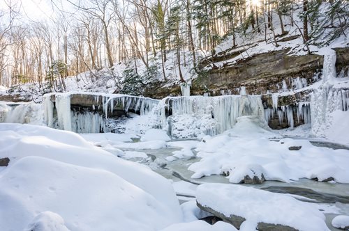 A stunning frozen waterfall in a wooded area, framed by trees and rocks, illustrating the calmness of a winter scene.