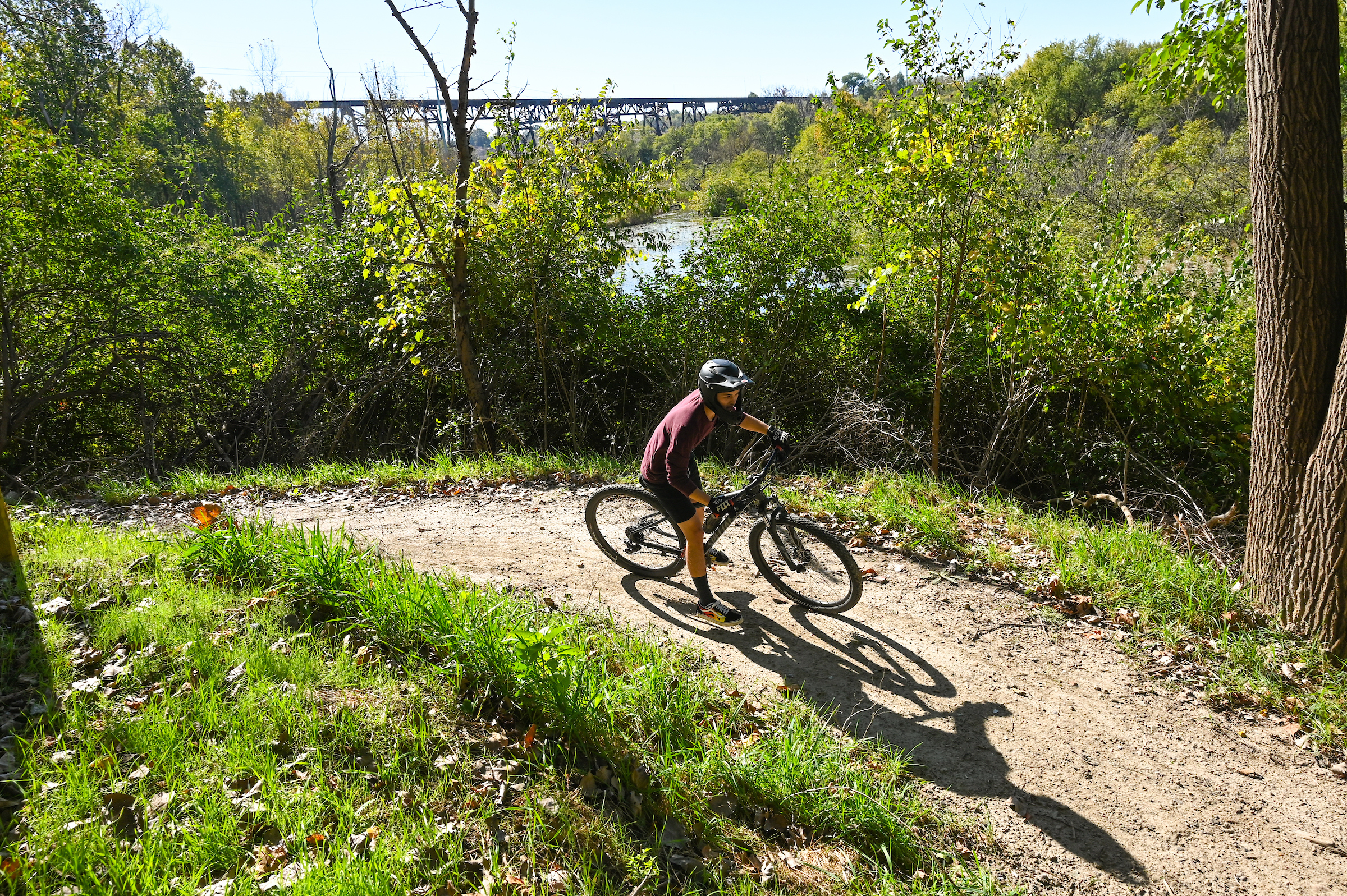 A cyclist pedals along a riverbank trail, immersed in the serene landscape and the gentle sounds of flowing water.