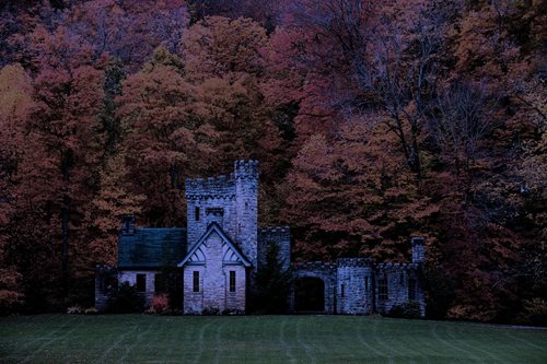 An ancient castle stands majestically in a vast, open field, surrounded by greenery and a clear blue sky.