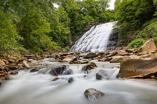 A stunning waterfall tumbles over stones, enveloped by verdant plants and the beauty of the natural landscape.