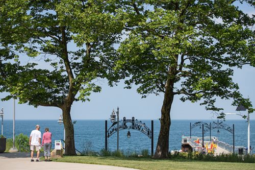 A couple strolls hand in hand along a scenic path beside the tranquil water, enjoying a peaceful moment together.