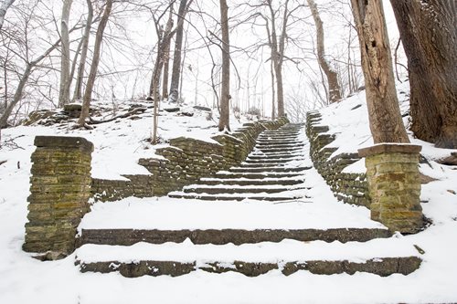 A winding stone staircase leads upward to a snow-covered hill, evoking a tranquil winter scene.