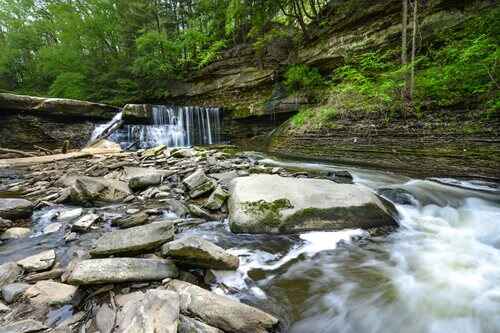 Water tumbles gracefully over rocks in a riverbed, creating a tranquil scene of a flowing waterfall in a natural setting.