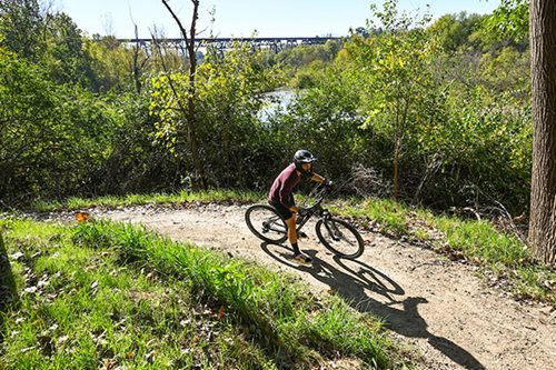 A cyclist navigates a scenic trail alongside a flowing river, enjoying the outdoors and the beauty of nature.