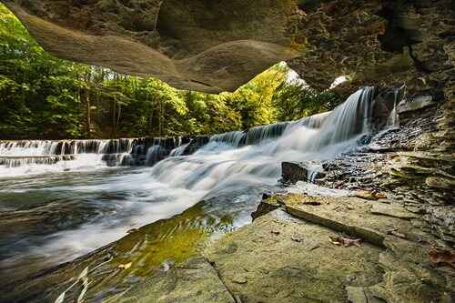 A beautiful waterfall tumbles through a cave, nestled in the woods, showcasing nature's serene beauty.