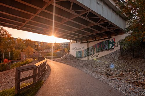 A tranquil bike path located under a bridge, with a stunning sunset casting vibrant colors across the scene.