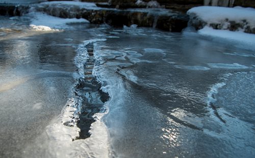 A frozen pond with a layer of ice glistening on the water, showcasing the beauty of winter's stillness.