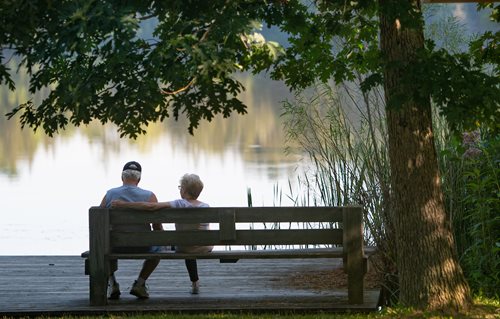 there are two people sitting on a bench by the water, a stock photo by Doug Ohlson, shutterstock contest winner, american romanticism, two old people, man and woman walking together, parks and lakes